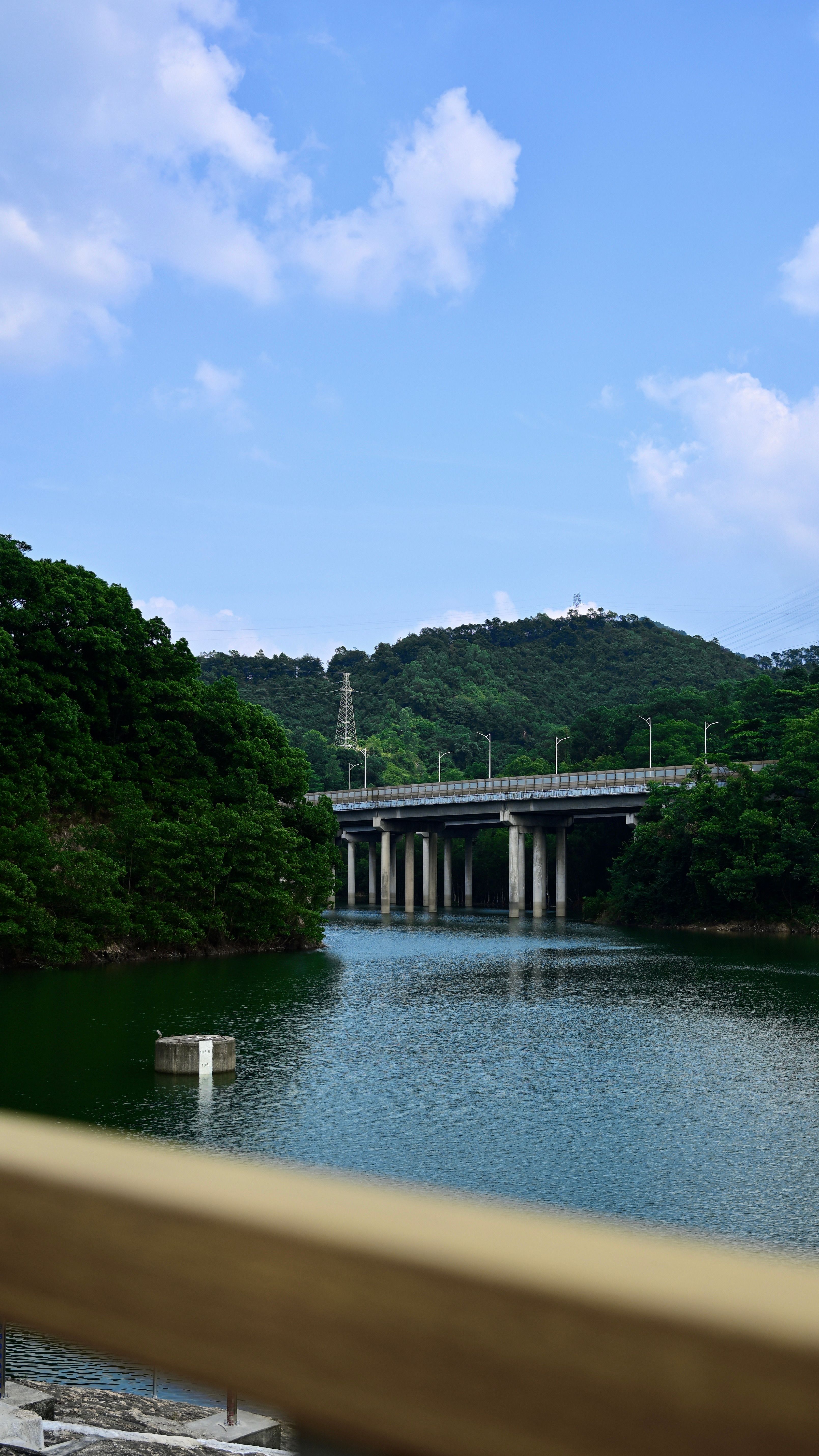 Beautiful view of a bridge over a tranquil river surrounded by lush green hills under a clear blue sky.
