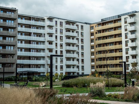 A modern apartment building surrounded by landscaped greenery under a cloudy sky.