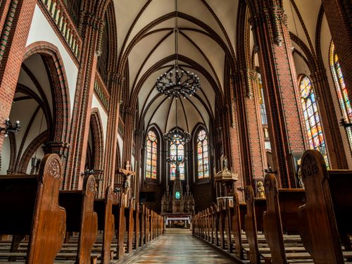 Free Intricate Gothic cathedral interior showcasing stained glass windows and wooden pews. Stock Photo