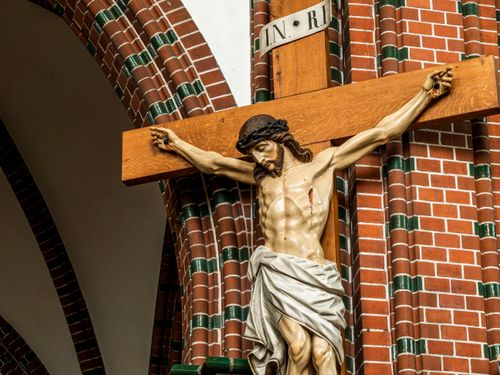 Free Crucifix sculpture of Jesus on the cross displayed in a brick church interior. Stock Photo