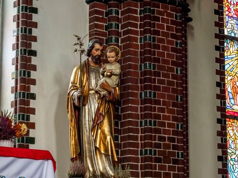 A statue of a saint holding a child in a church with stained glass in the background.
