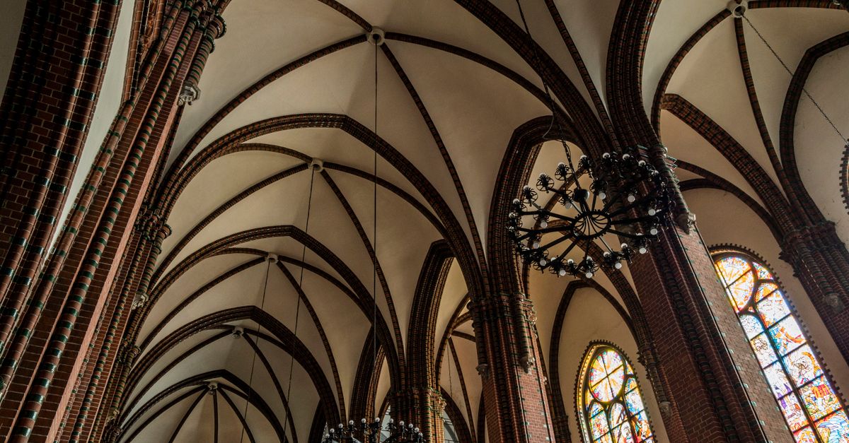 Interior view of a gothic cathedral featuring vaulted ceilings and colorful stained glass windows.