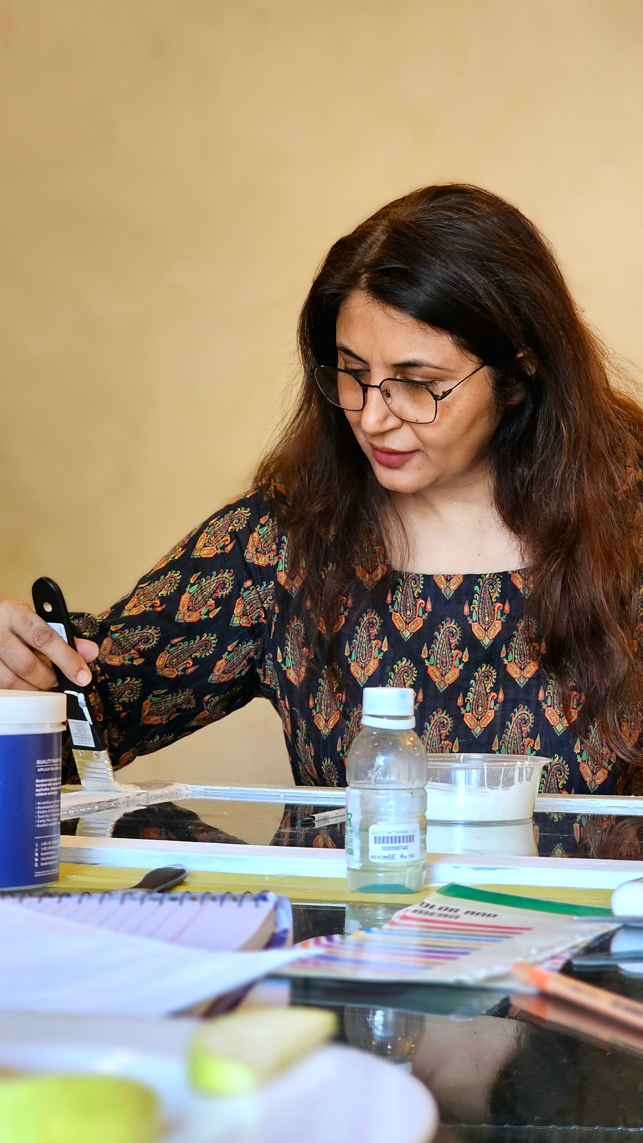 Woman focused on creative painting project using various tools on desk.