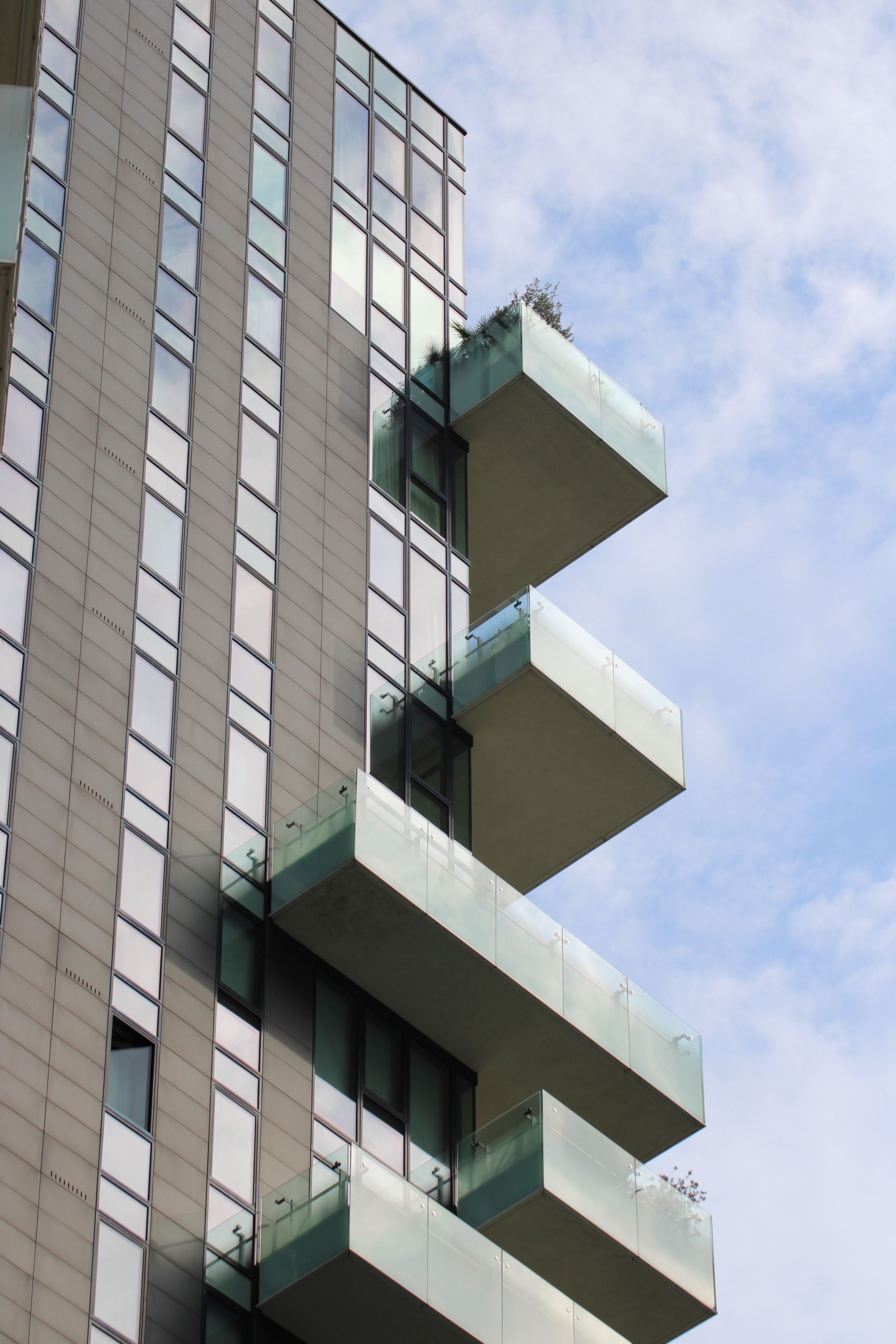Low-angle view of modern skyscraper in Milan, featuring distinctive glass balconies against a clear blue sky.