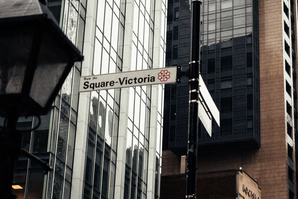 Street sign for Rue du Square-Victoria in Montreal, set against a backdrop of modern architecture.