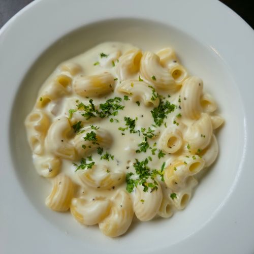 Free Delicious creamy macaroni pasta served in a white bowl, garnished with fresh herbs. Stock Photo