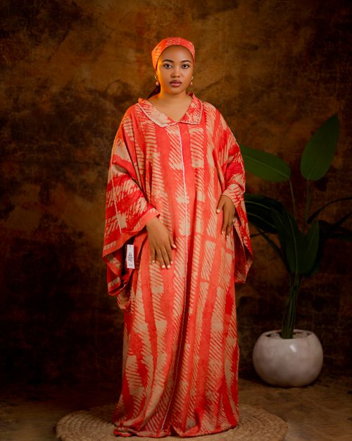 Free Portrait of a woman in a vibrant red kaftan with a plant backdrop indoors. Stock Photo