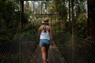 一位戴着帽子的女人悠闲地走过森林中一座木制吊桥