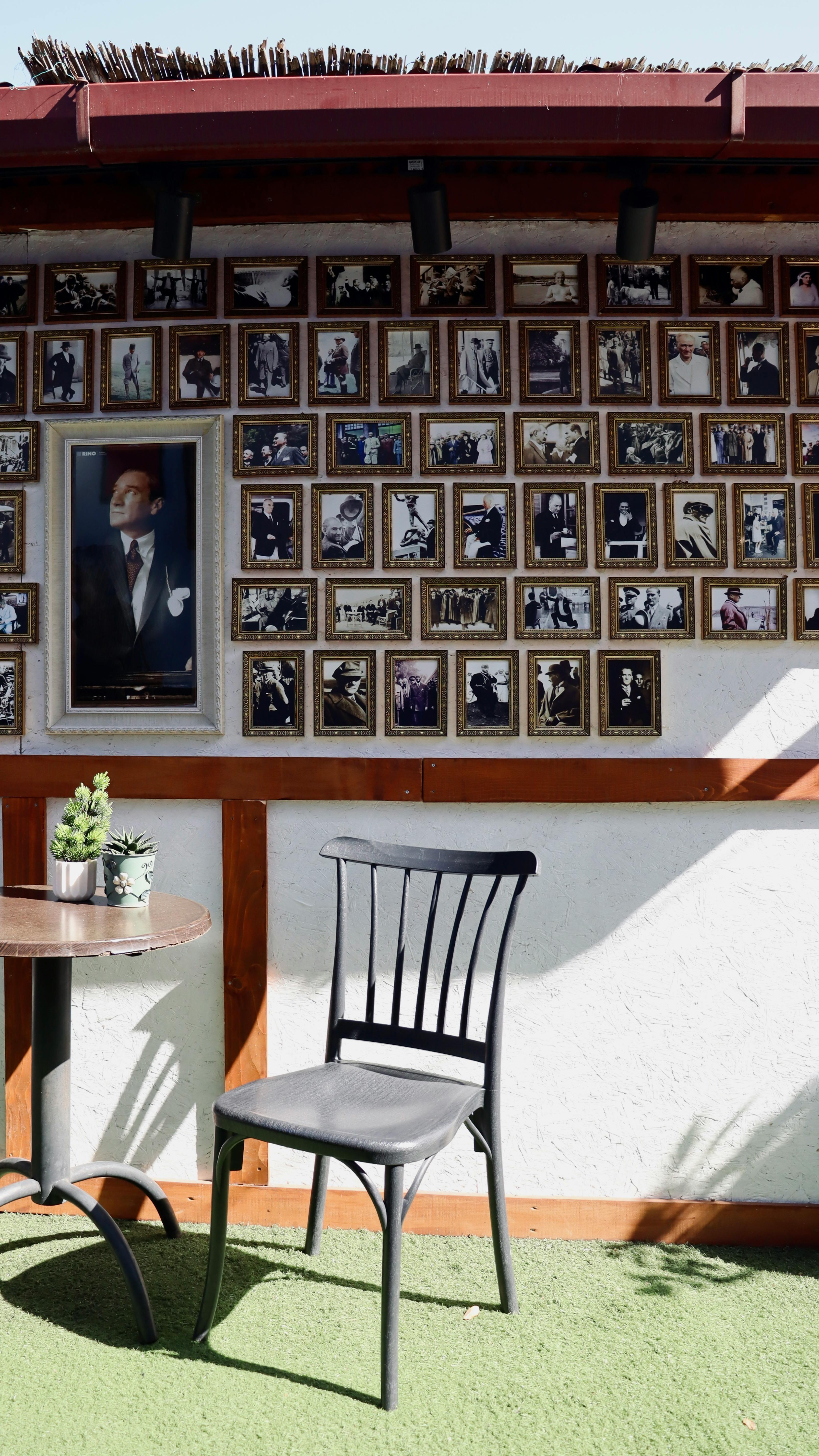 Sunlit outdoor wall with numerous photo frames, table, and chair.