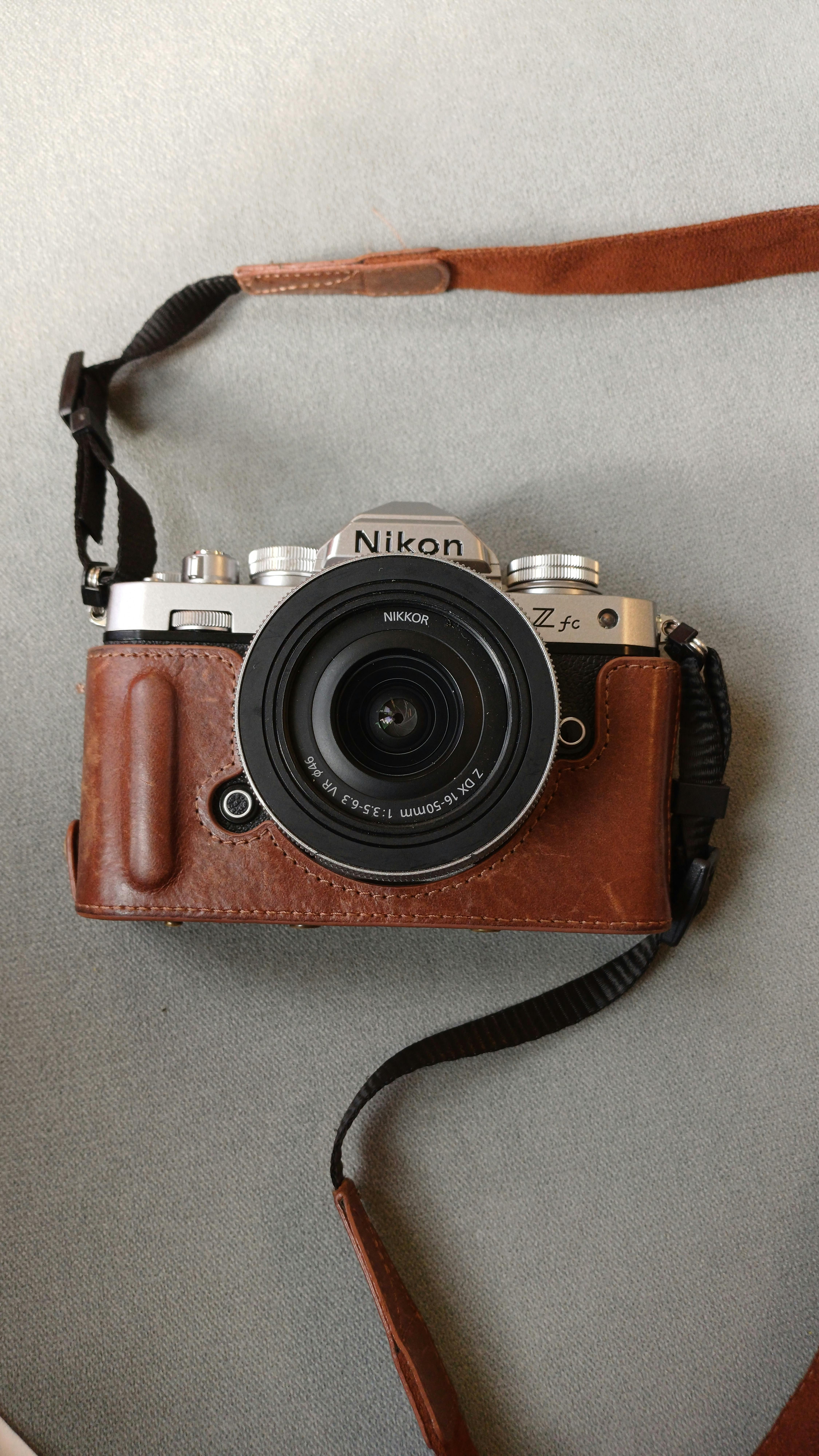 Klasický bezzrcadlový fotoaparát v hnědém koženém pouzdře na neutrálním pozadí. Ideální pro nadšence fotografie.