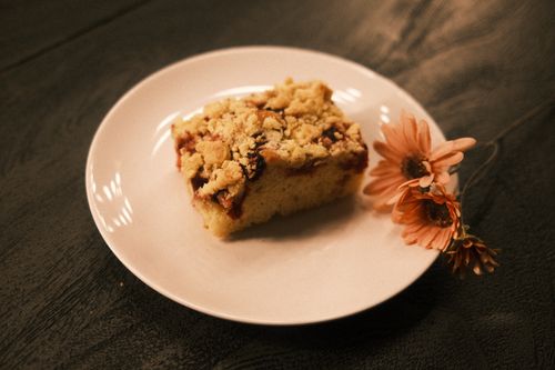 Free A piece of crumb-topped cake on a white plate with pink flowers for decoration. Stock Photo
