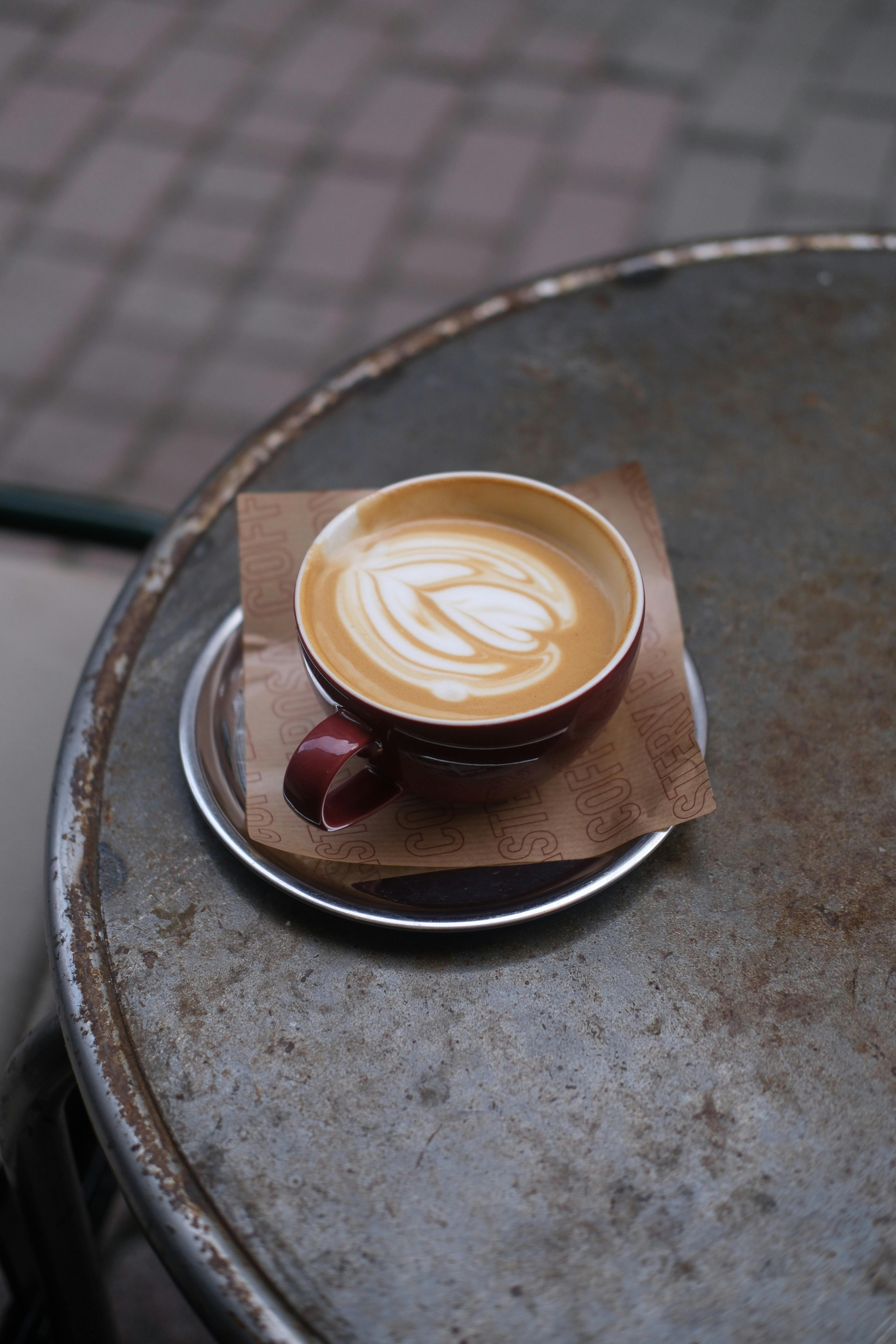 A beautifully crafted latte with art served in a red cup on a rustic metal table.