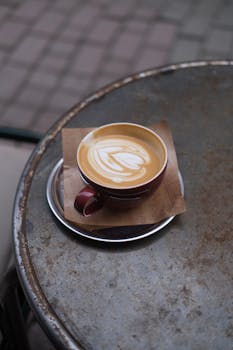 A beautifully crafted latte with art served in a red cup on a rustic metal table.