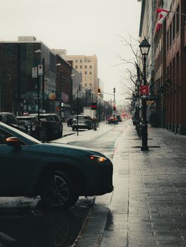 A rainy day in downtown Montreal with cars on a wet street and Canadian flags.