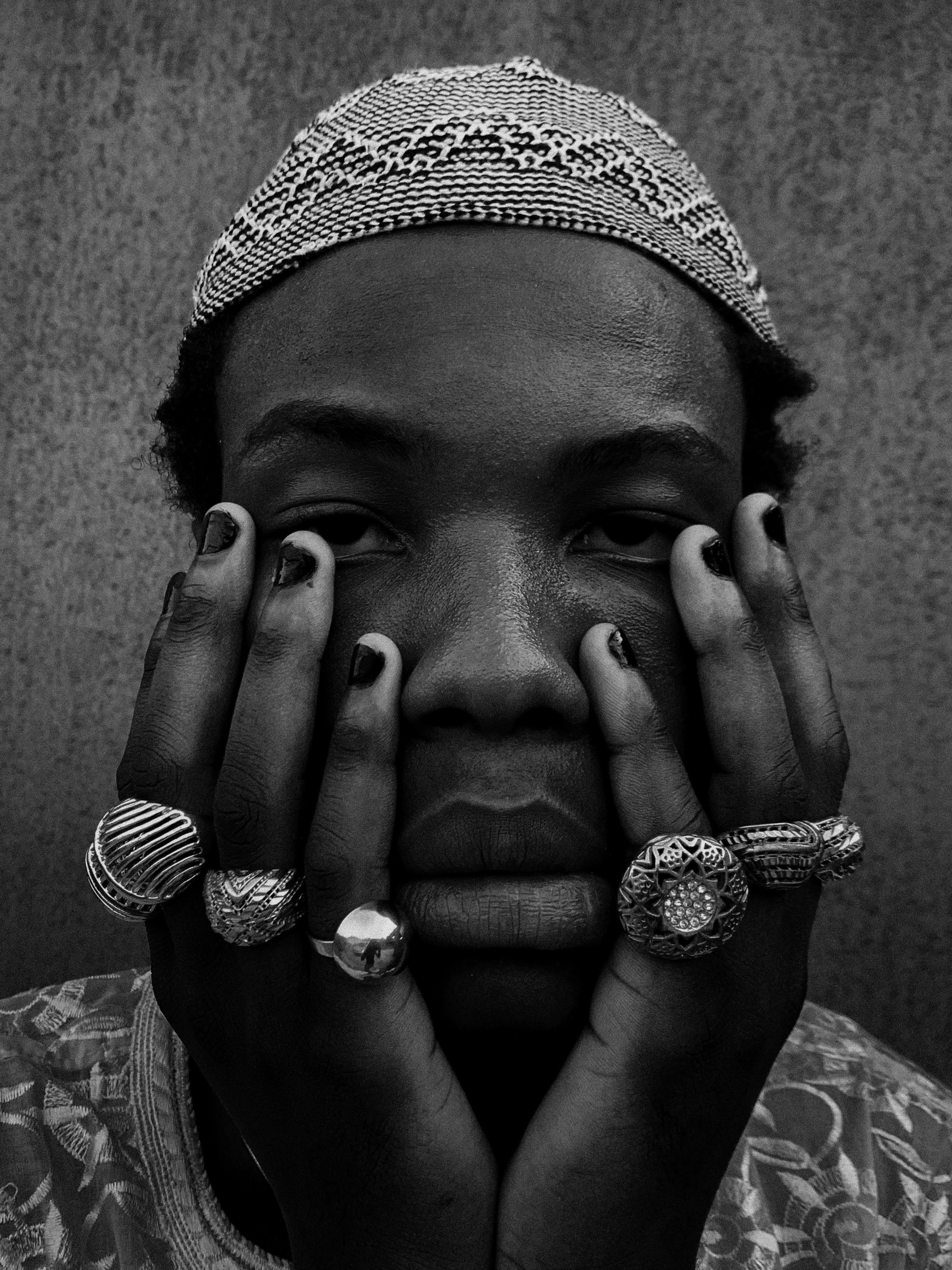 Black and white portrait of a man wearing rings and a traditional cap, conveying deep emotion.