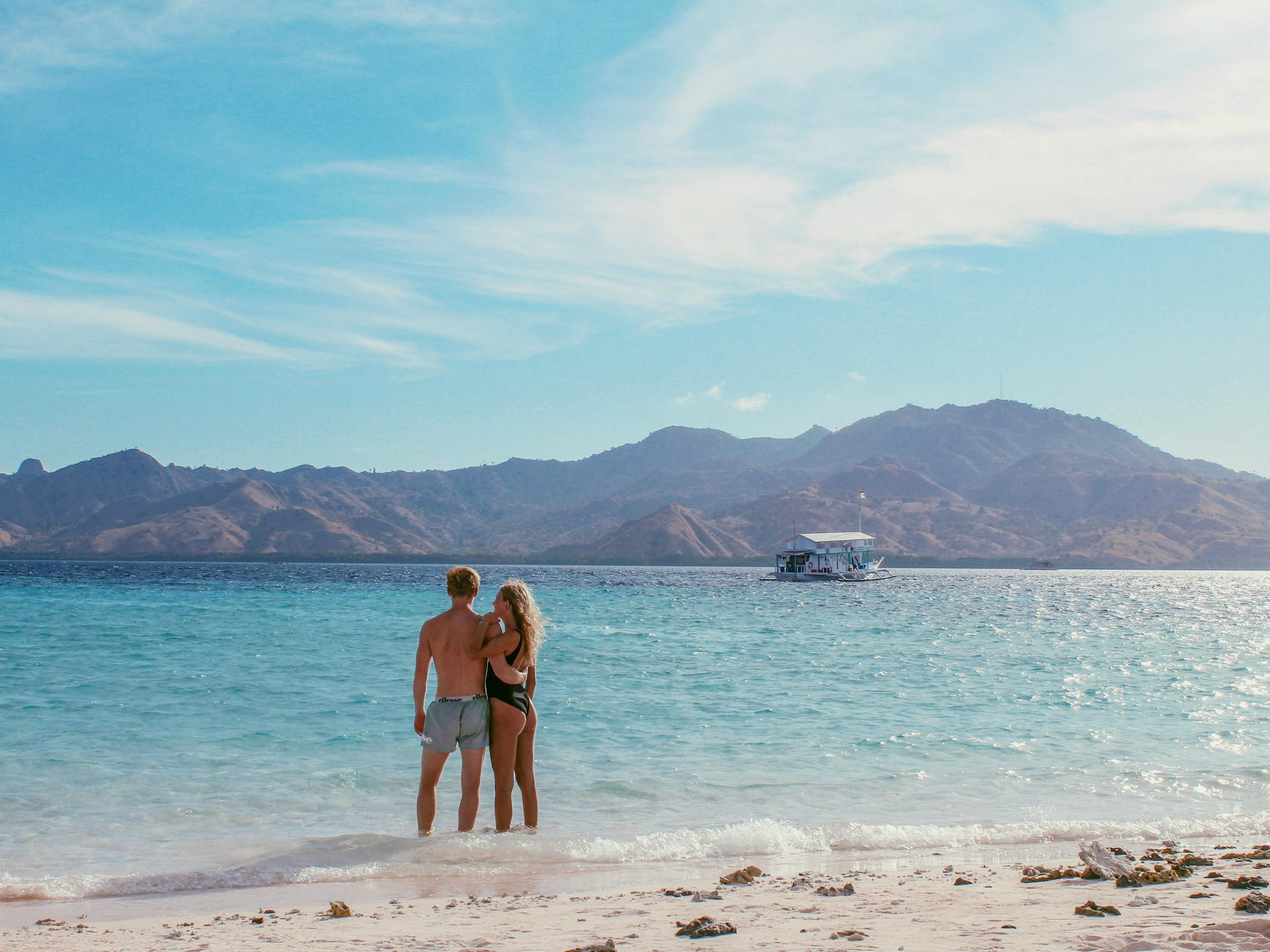 A couple enjoying a tropical beach in East Nusa Tenggara with mountains in the background.