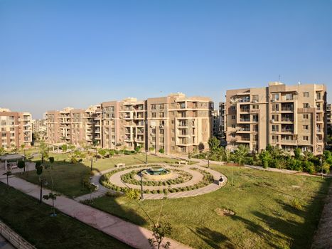 Aerial view of a modern apartment complex featuring a central landscaped garden on a sunny day.