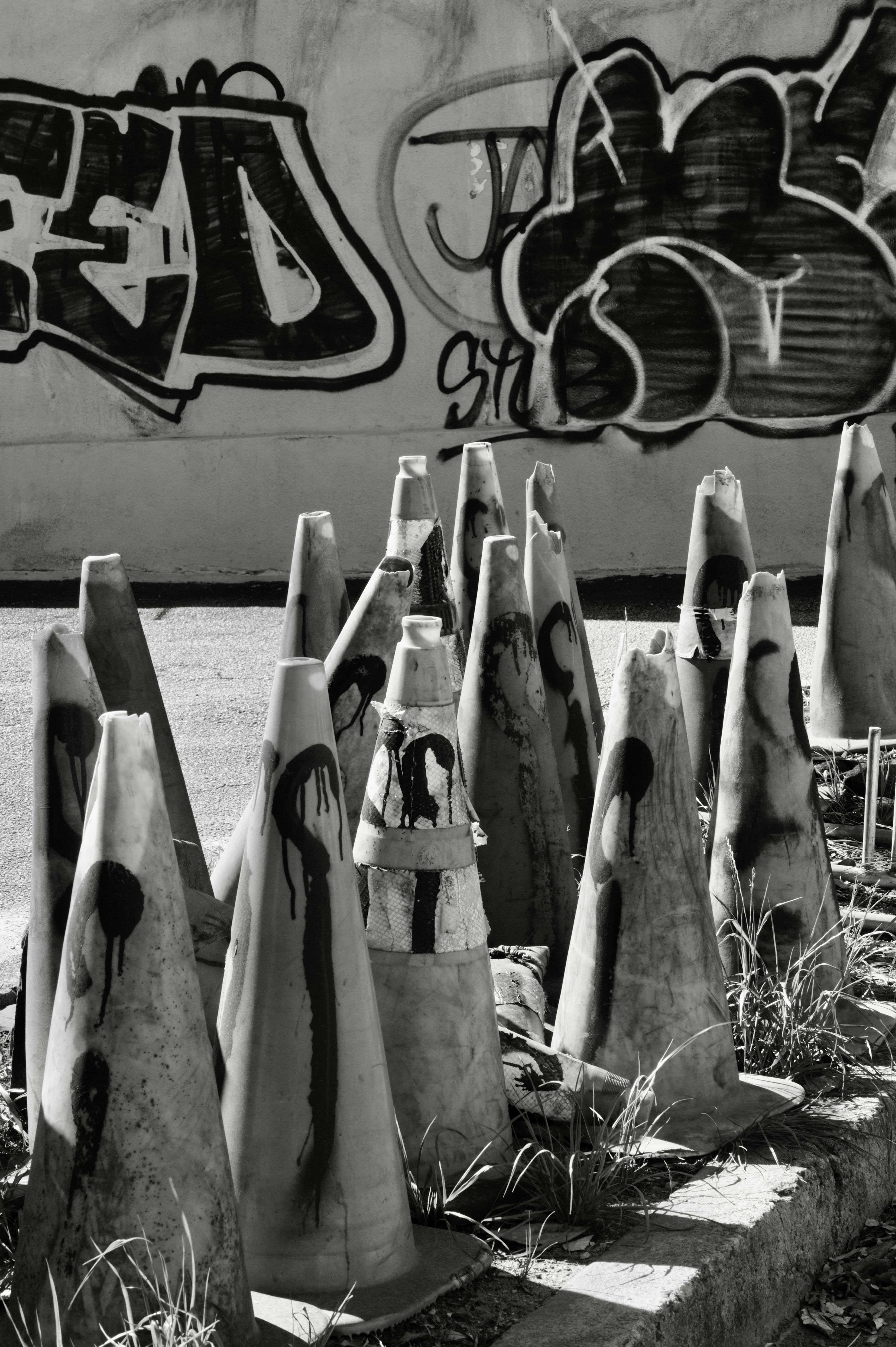 Black and white photo of painted traffic cones against graffiti wall.