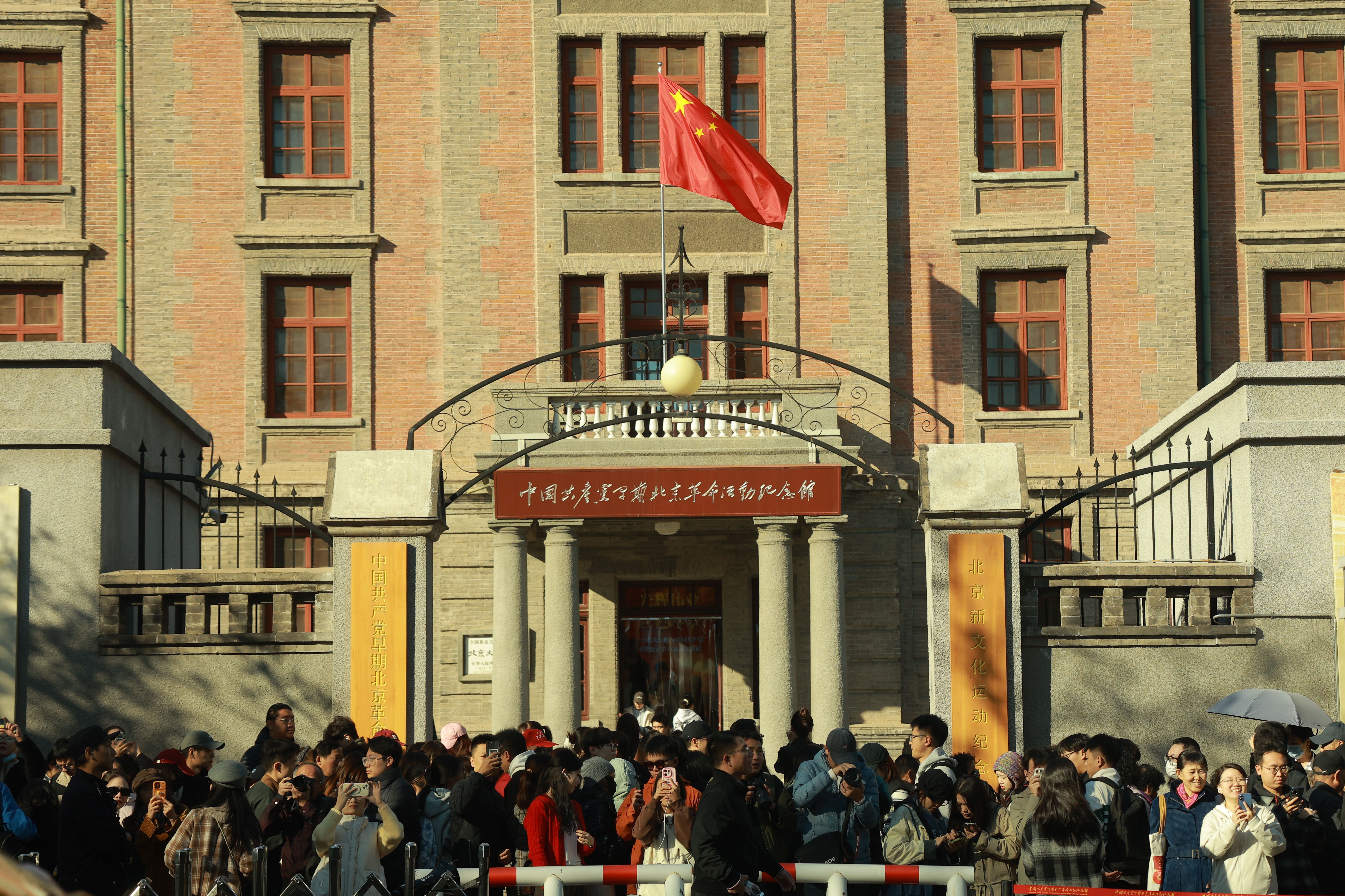 Large crowd gathers at Beijing museum entrance under a Chinese flag, sunny day.