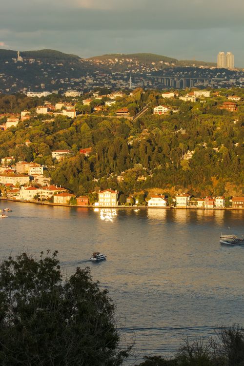Free View of a sunlit coastal town with boats on the water under a clouded sky. Stock Photo