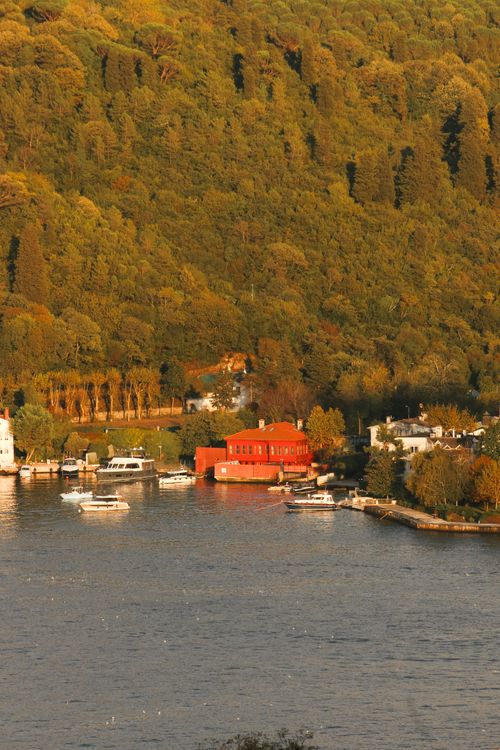 Free Picturesque riverside with boats and a vibrant red building amid lush greenery. Stock Photo