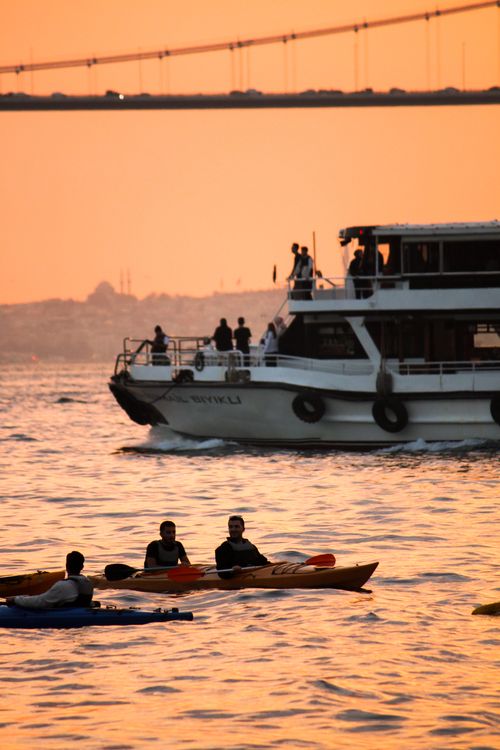 Free Serene sunset boating scene with kayaks and a boat on calm waters near a bridge. Stock Photo