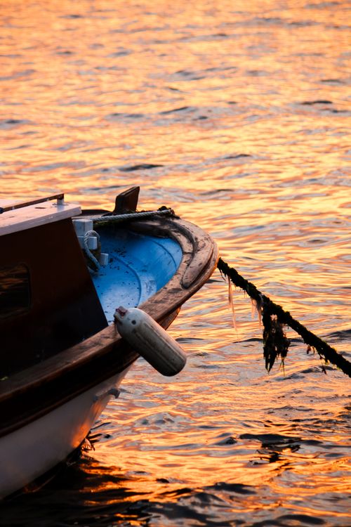 Free A tranquil boat rests on shimmering golden waters during sunset, creating a peaceful scene. Stock Photo