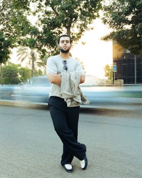 Confident man with sunglasses standing on street with blurred motion cars behind in urban setting.