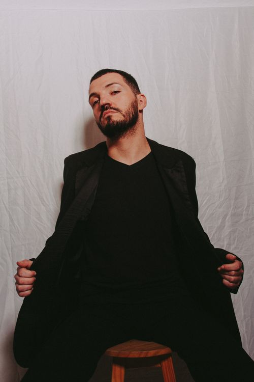 Free Portrait of a confident man in a black suit posing on a stool with a white backdrop. Stock Photo