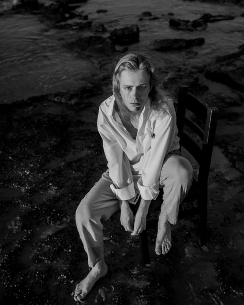 Free Artistic black and white portrait of a pensive adult on a chair by the beach at dusk. Stock Photo