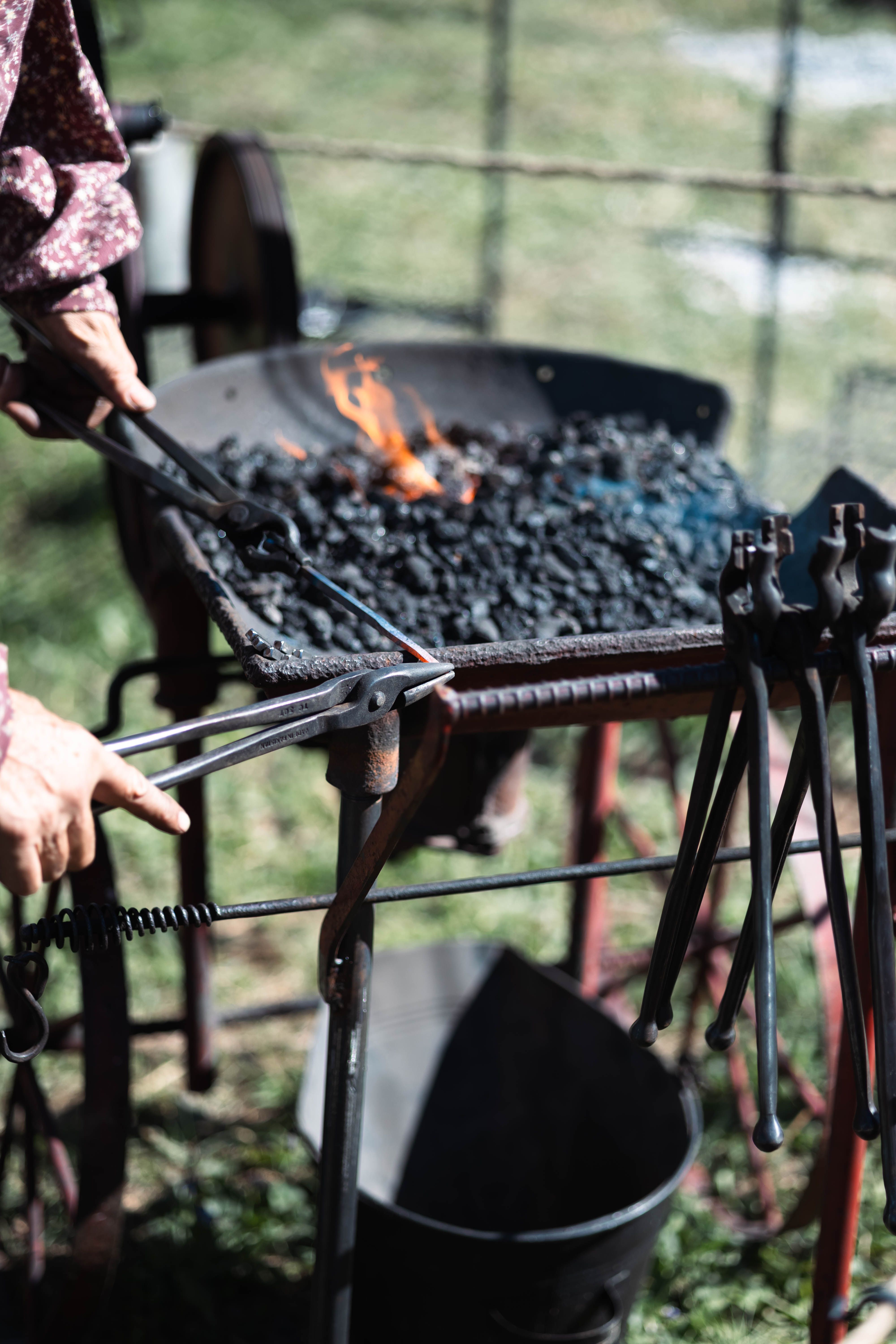 A traditional blacksmith working outdoors with tools and a glowing forge.