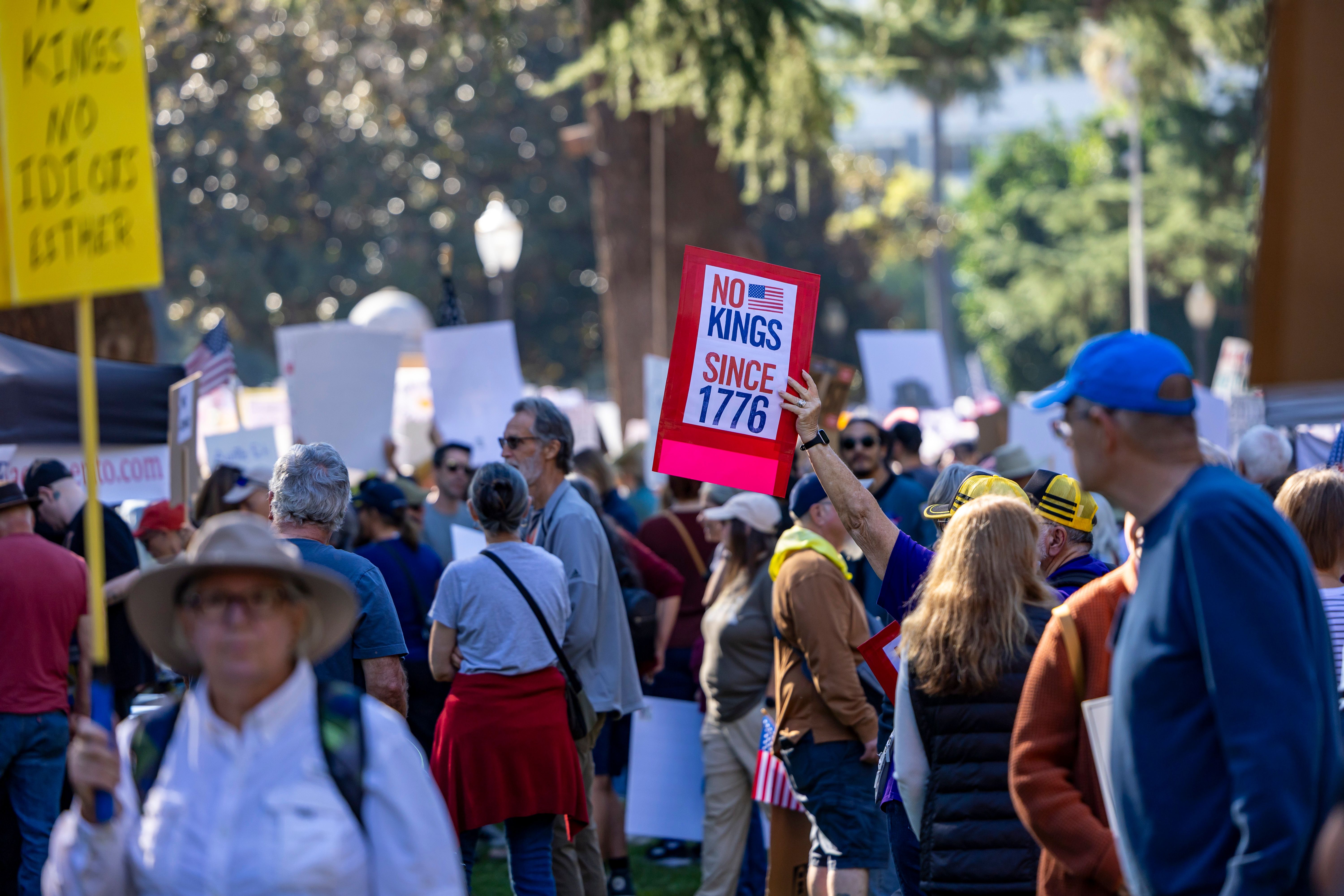 A diverse crowd gathers in Sacramento for a protest, holding signs with messages about independence and governance.