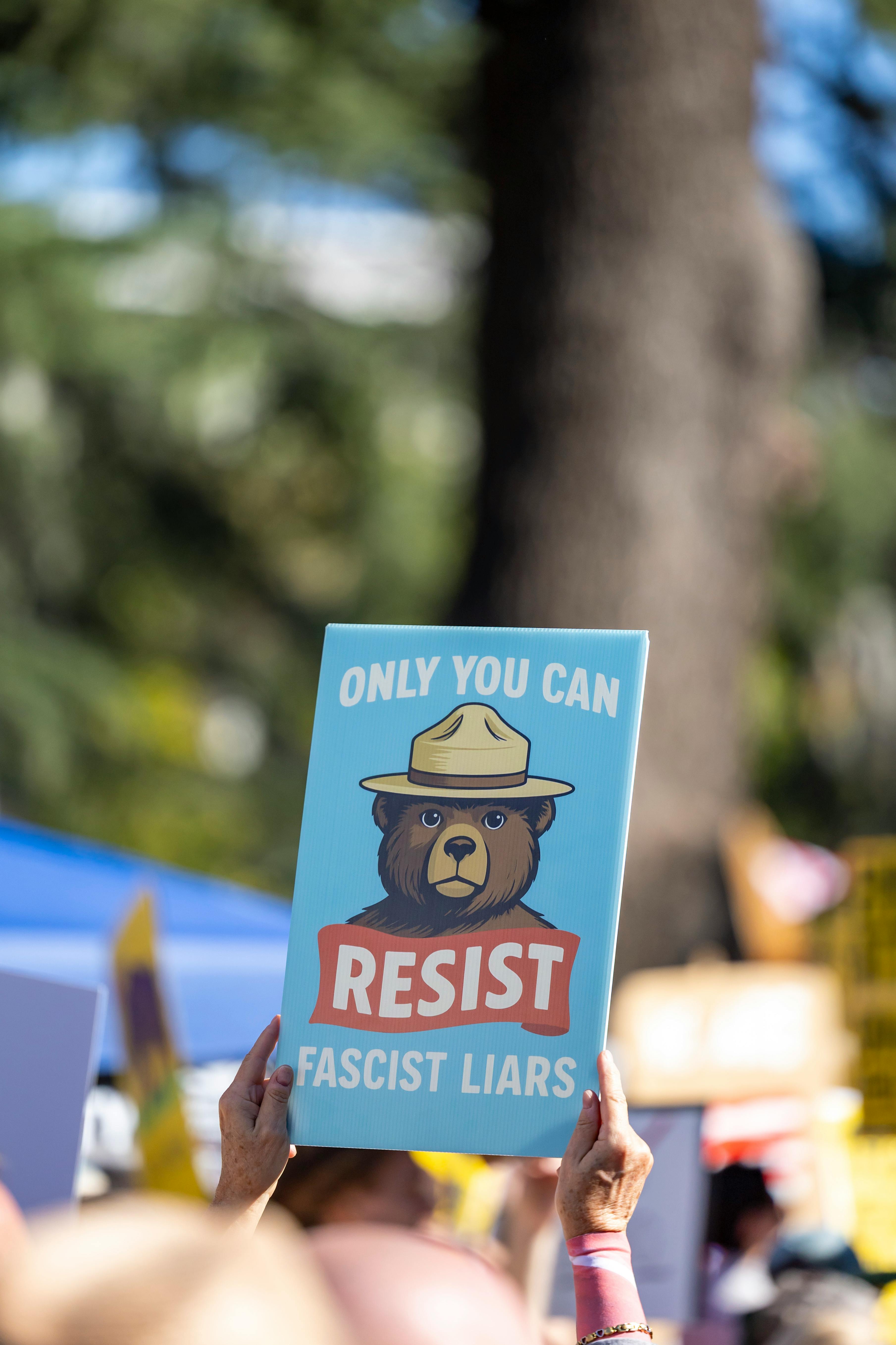 A protest sign depicting Smokey Bear with the text 'Resist Fascist Liars' at a rally in Sacramento.