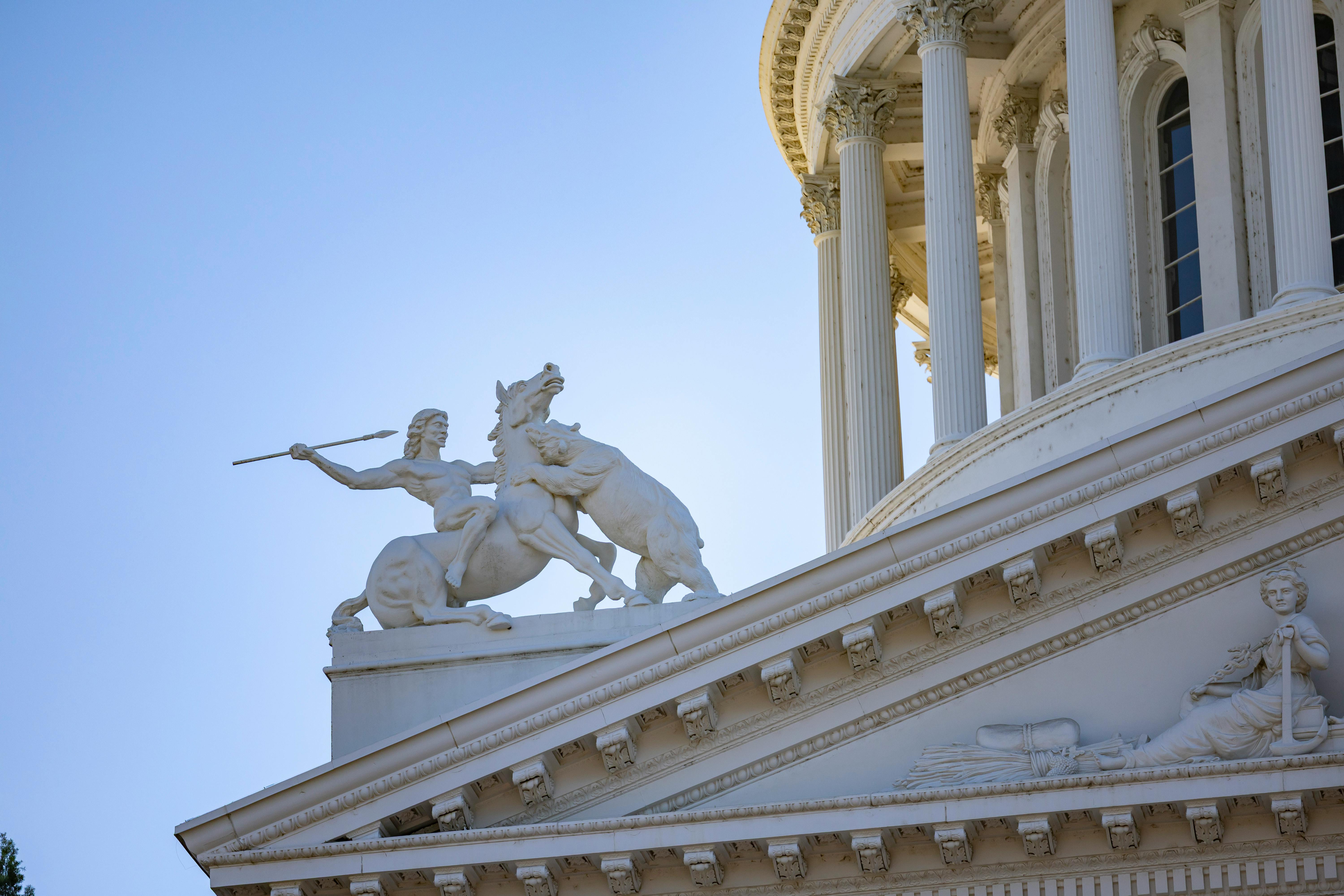 Close-up of a historical statue on the Sacramento State Capitol building with clear blue sky.
