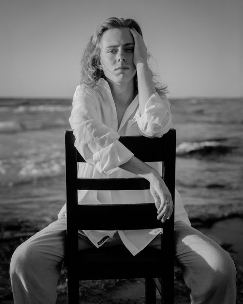 Free Black and white portrait of a contemplative person sitting by the ocean in the evening. Stock Photo