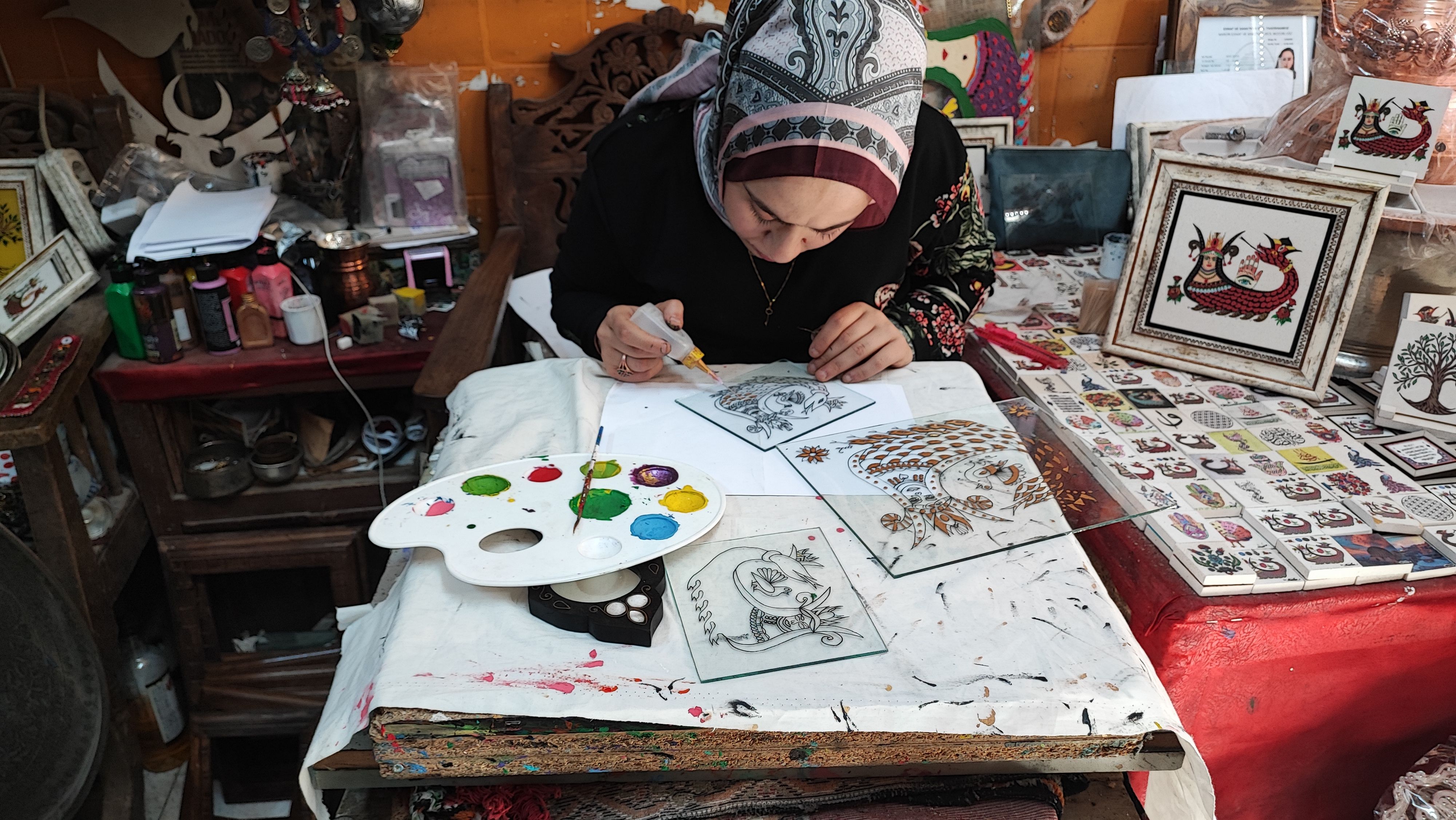 Woman in traditional attire painting detailed designs on glass in an art studio.