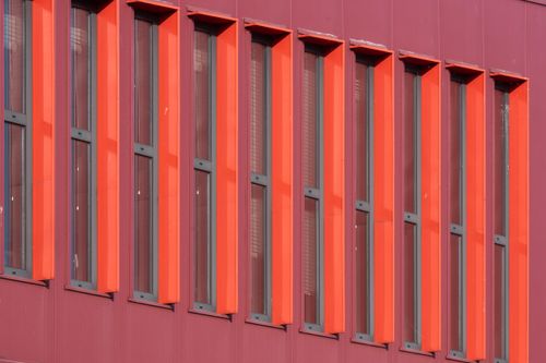 Free Close-up of a modern building facade with red and maroon vertical windows, showcasing architectural design. Stock Photo