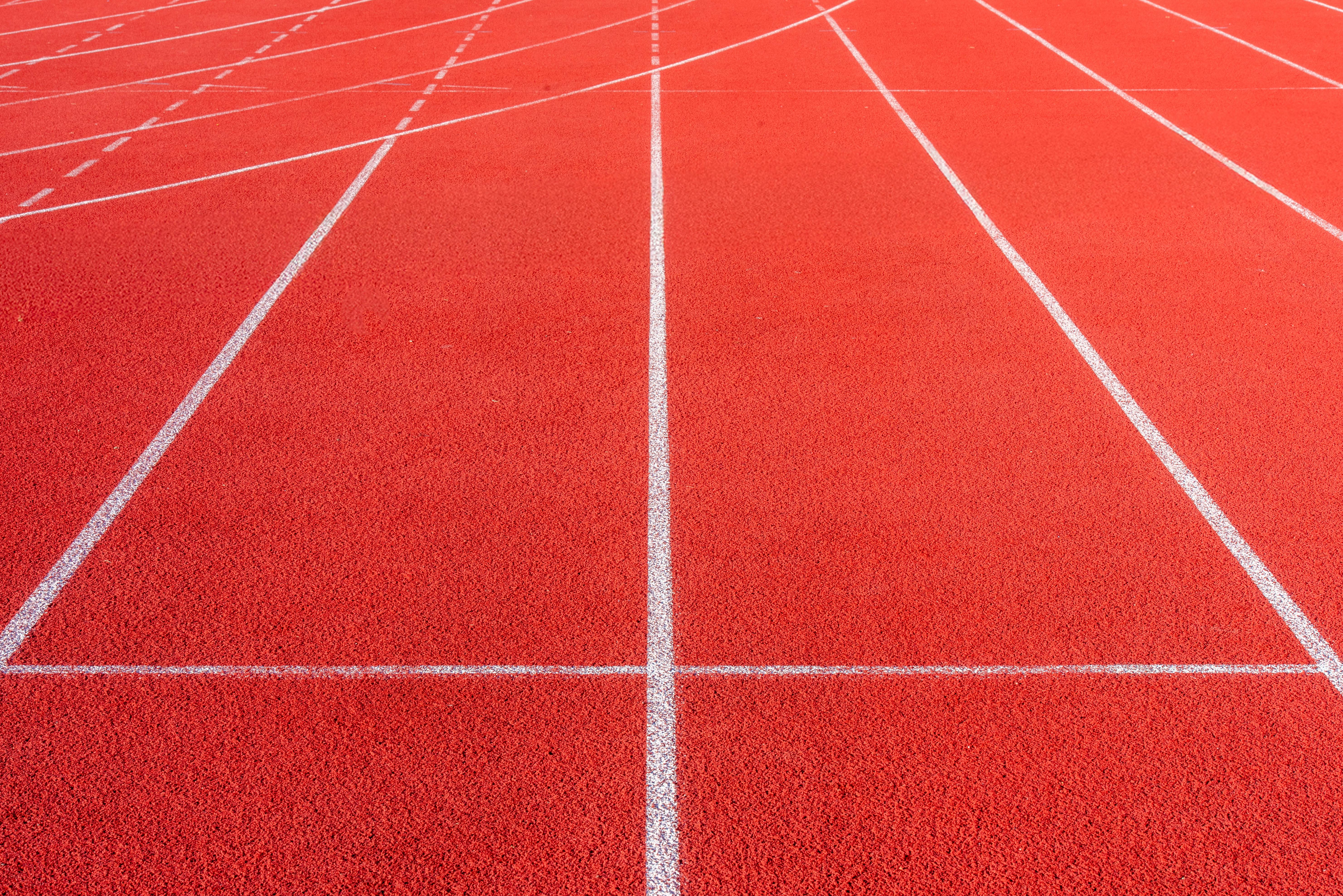 Vibrant red athletics track with distinct white lines creating dynamic patterns.