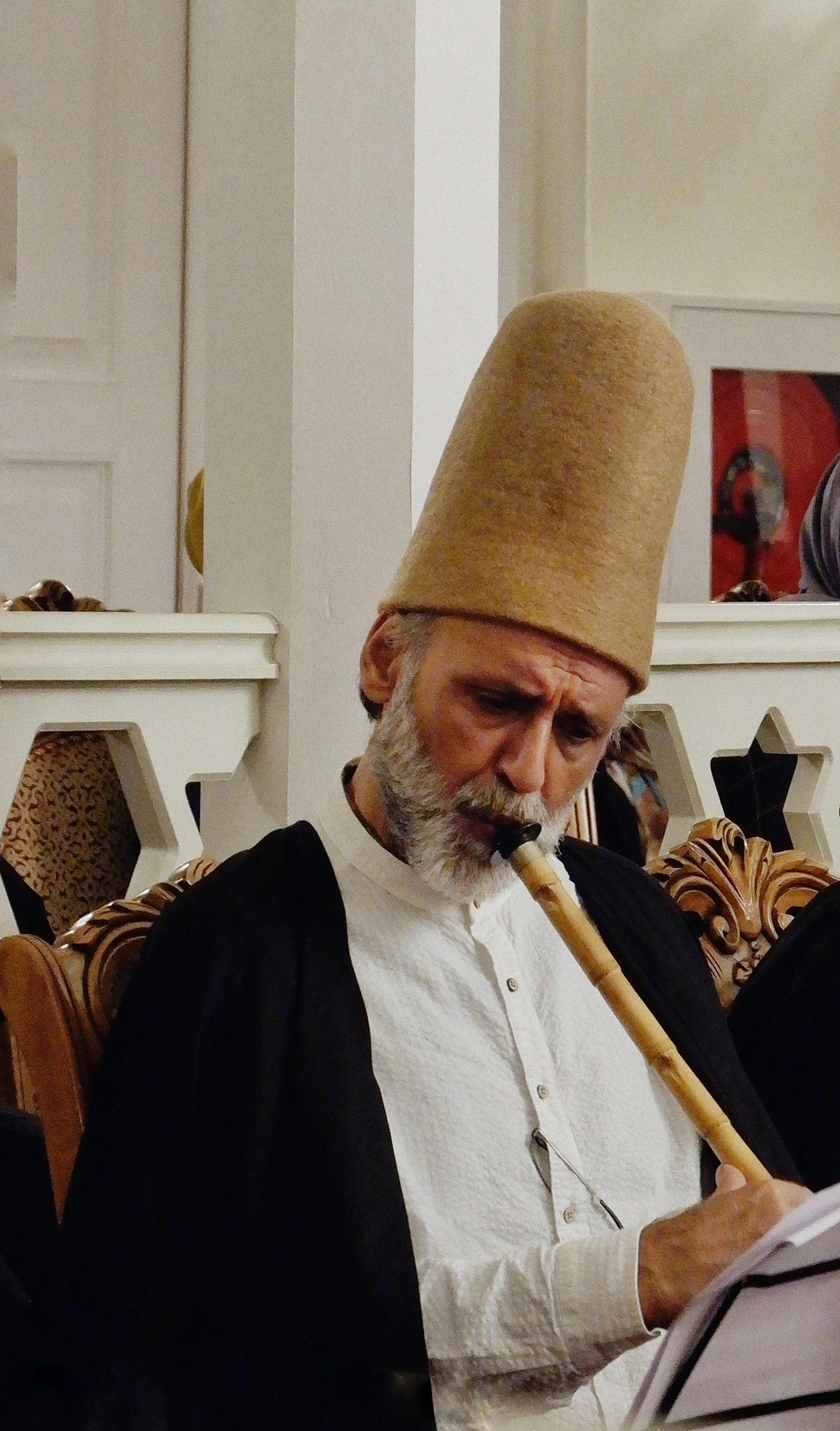 Sufi musician in traditional attire playing the Ney during a spiritual ceremony indoors.