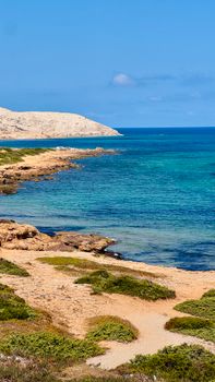 Tranquil coastal scene featuring clear blue waters and rocky shoreline under a bright blue sky.