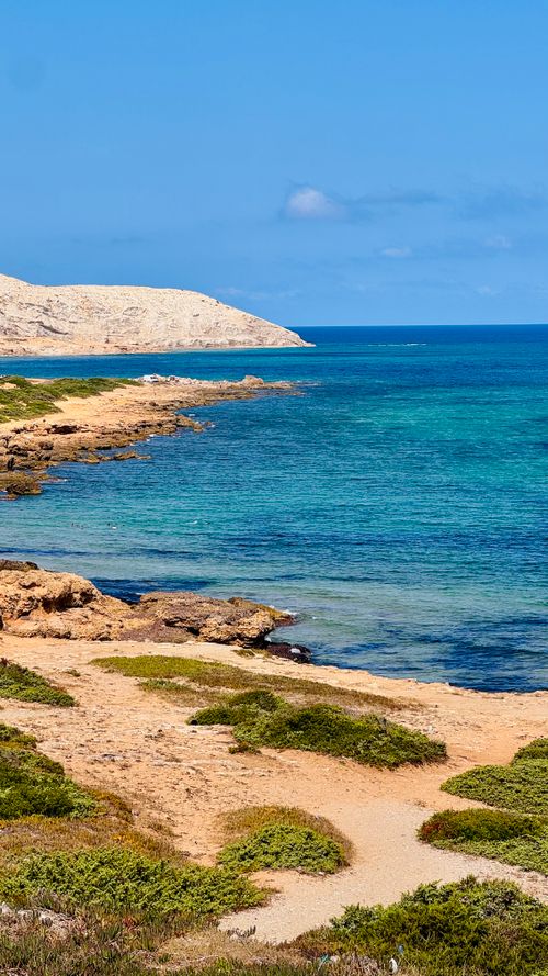 Free Tranquil coastal scene featuring clear blue waters and rocky shoreline under a bright blue sky. Stock Photo