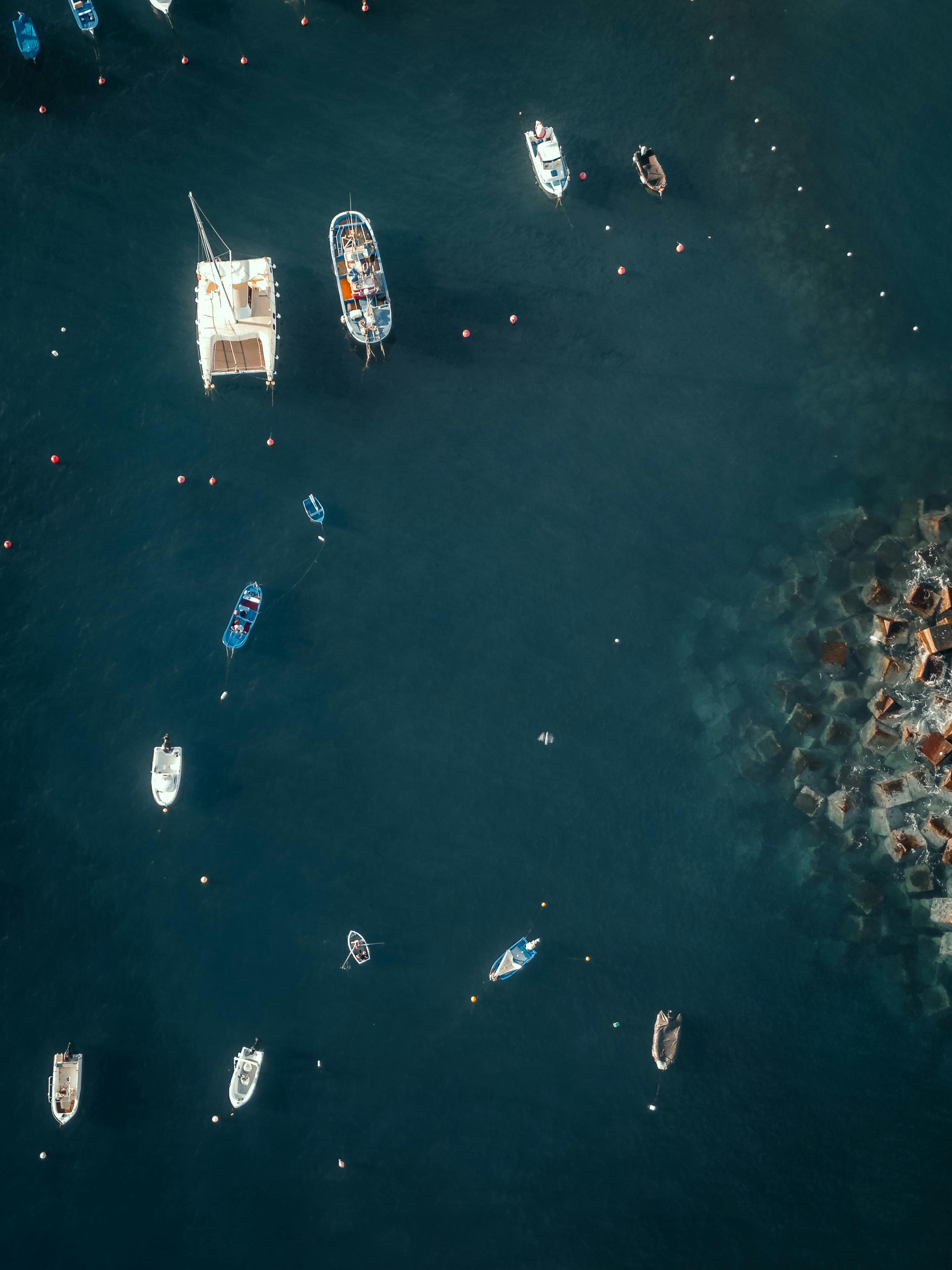 무료 바위 해안 근처의 깊고 푸른 바다에 떠 있는 다양한 보트를 평온하게 공중에서 촬영한 사진입니다. 스톡 사진