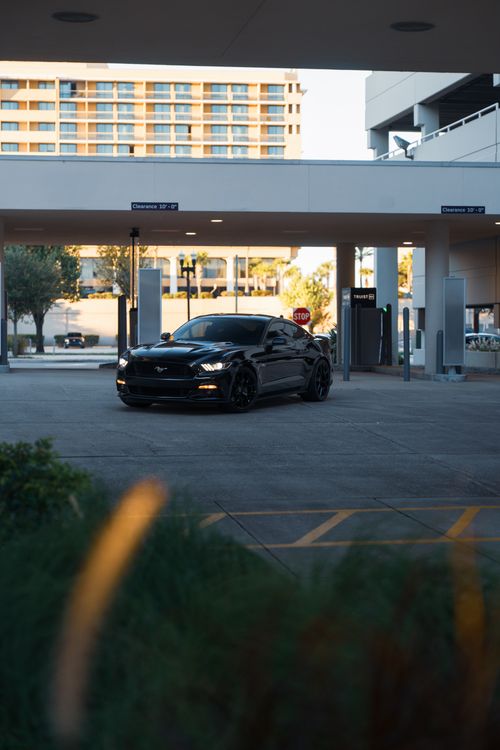 Free Black sporty car parked in a modern urban garage, highlighting sleek design and city architecture. Stock Photo
