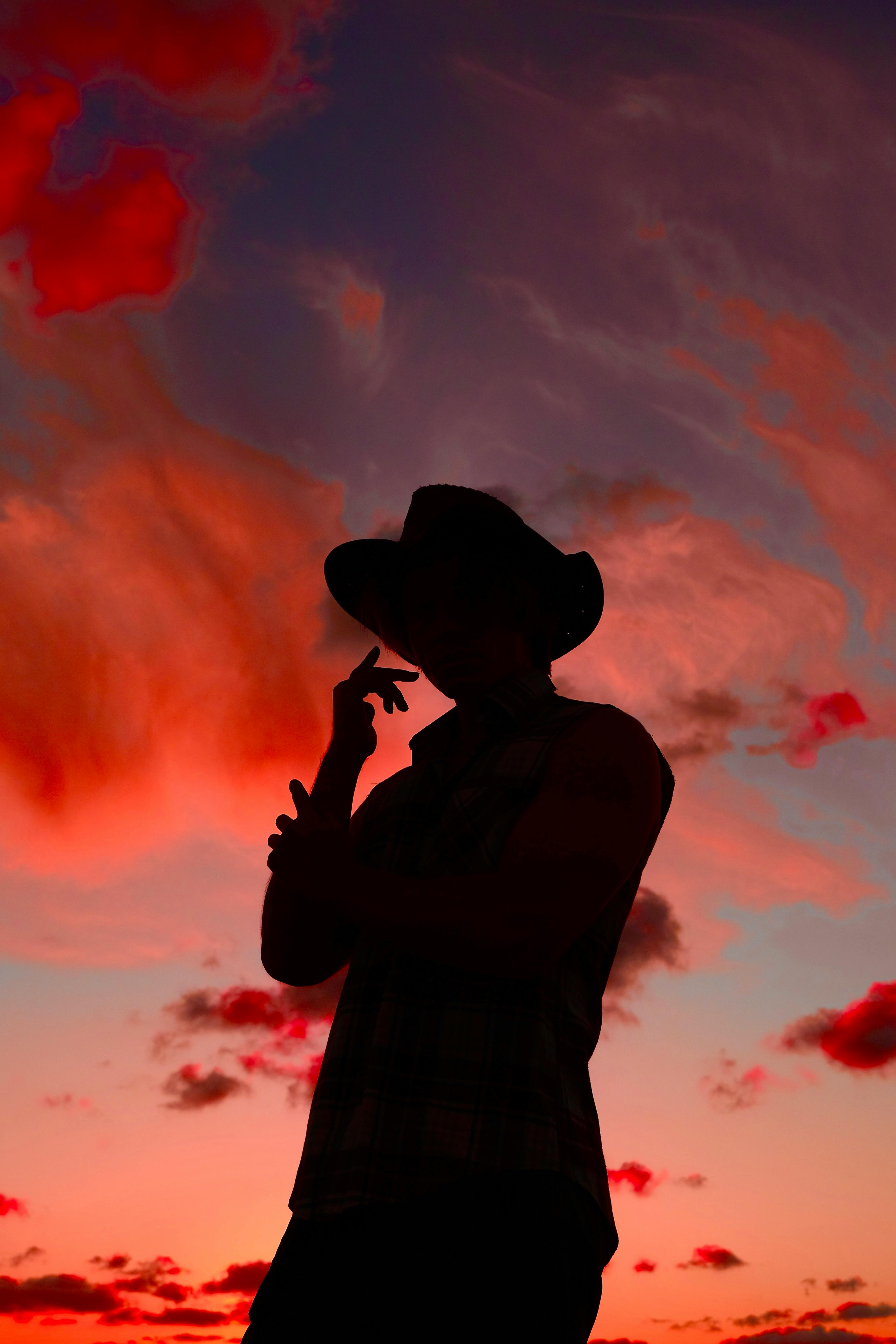 Silhouette of a man wearing a cowboy hat against a vivid red and orange sunset sky.