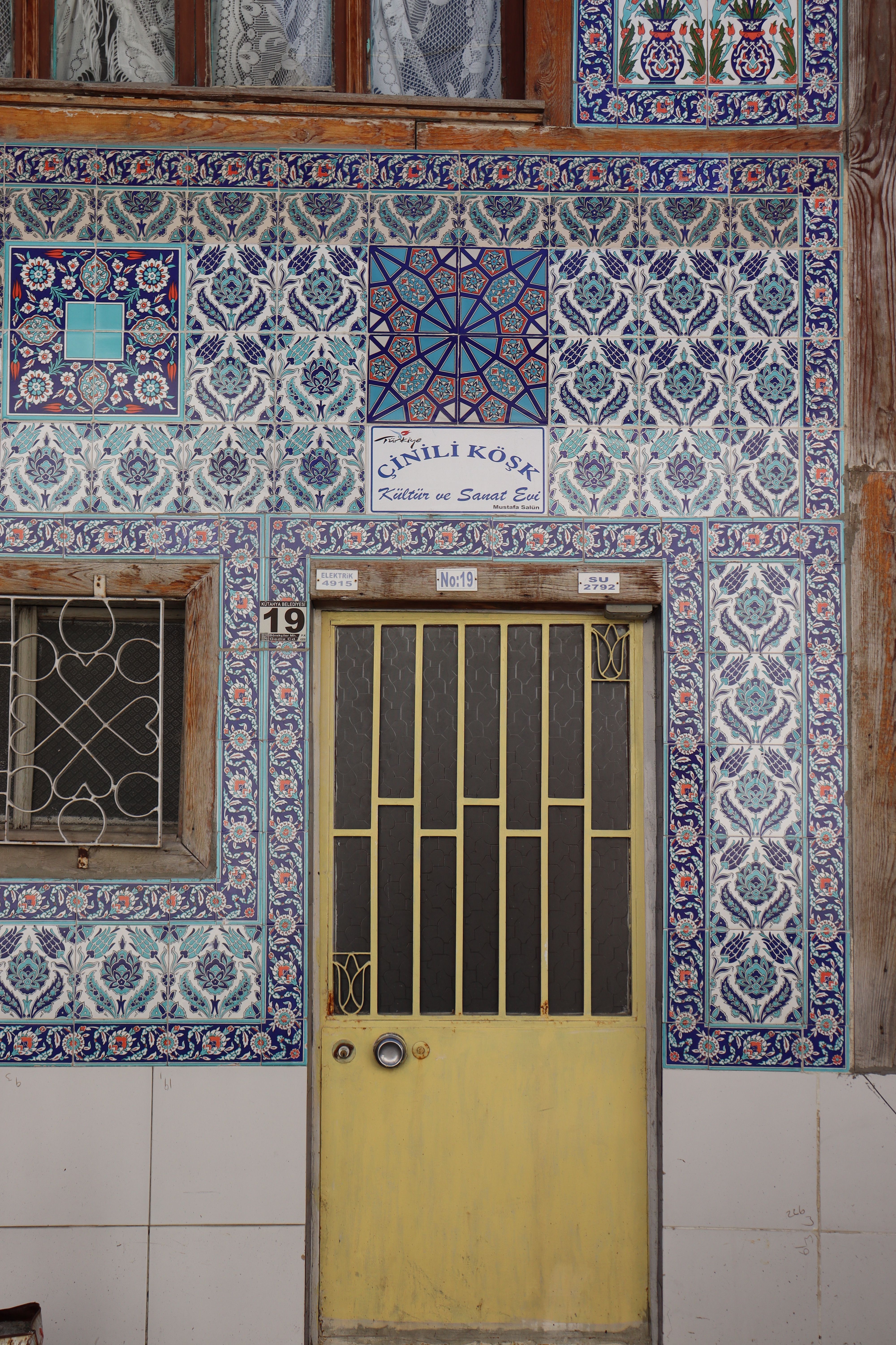 Vibrant traditional Turkish mosaic wall featuring a rustic yellow door in a quaint neighborhood.