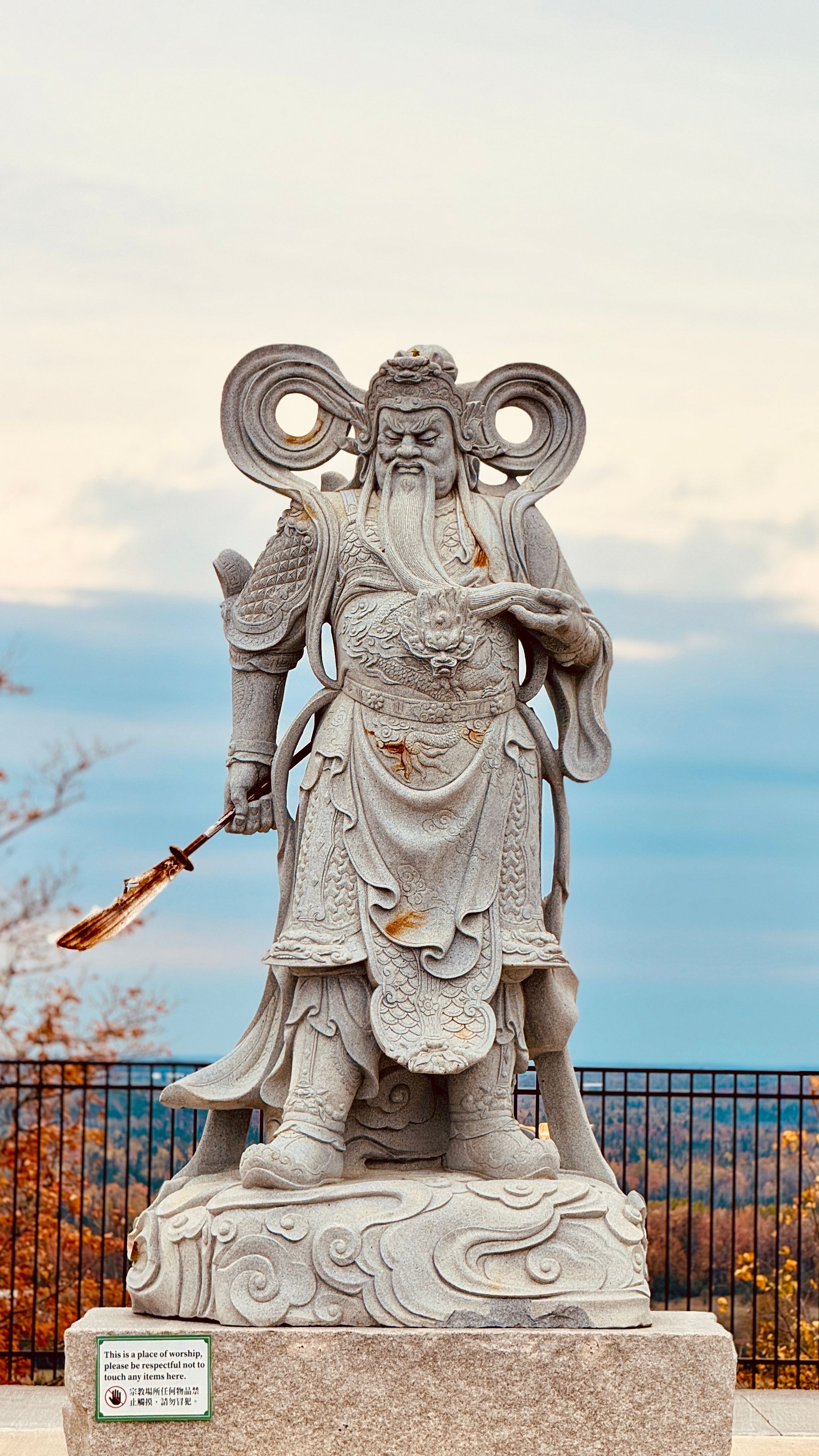 Intricately carved stone warrior statue in a serene outdoor setting with a vast horizon backdrop.