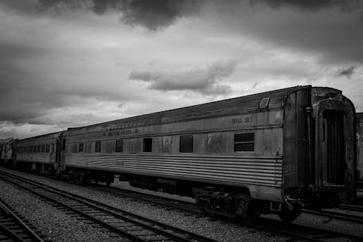 A timeless black and white image of a vintage train on the tracks under a cloudy sky.