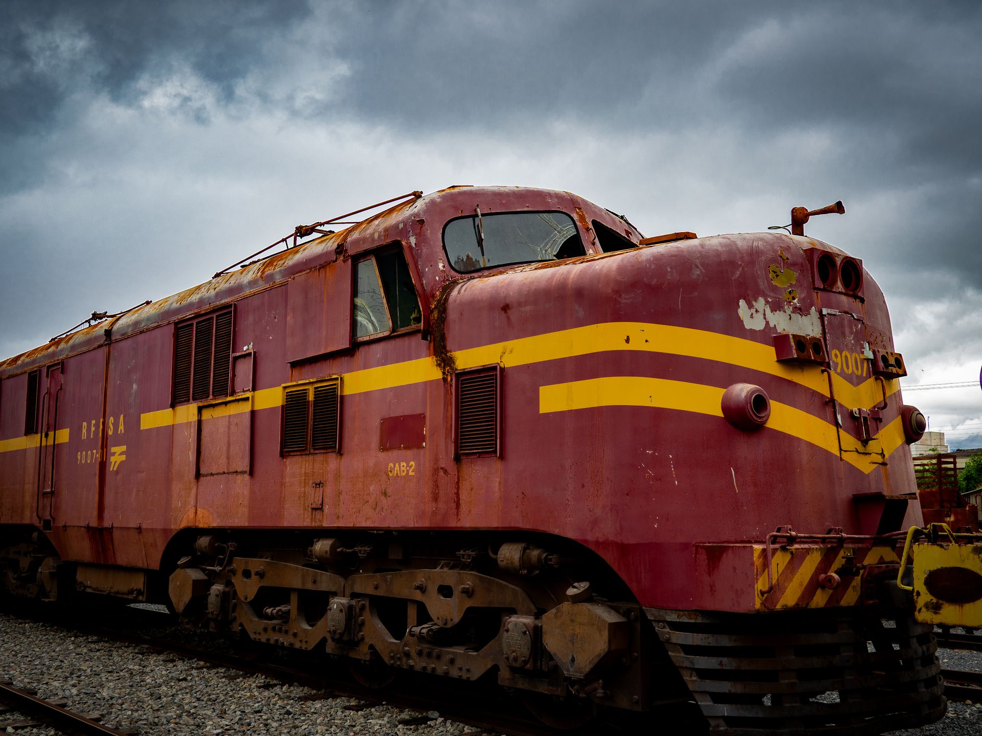 Aged locomotive with rust and weathered paint, standing under a dark, cloudy sky.