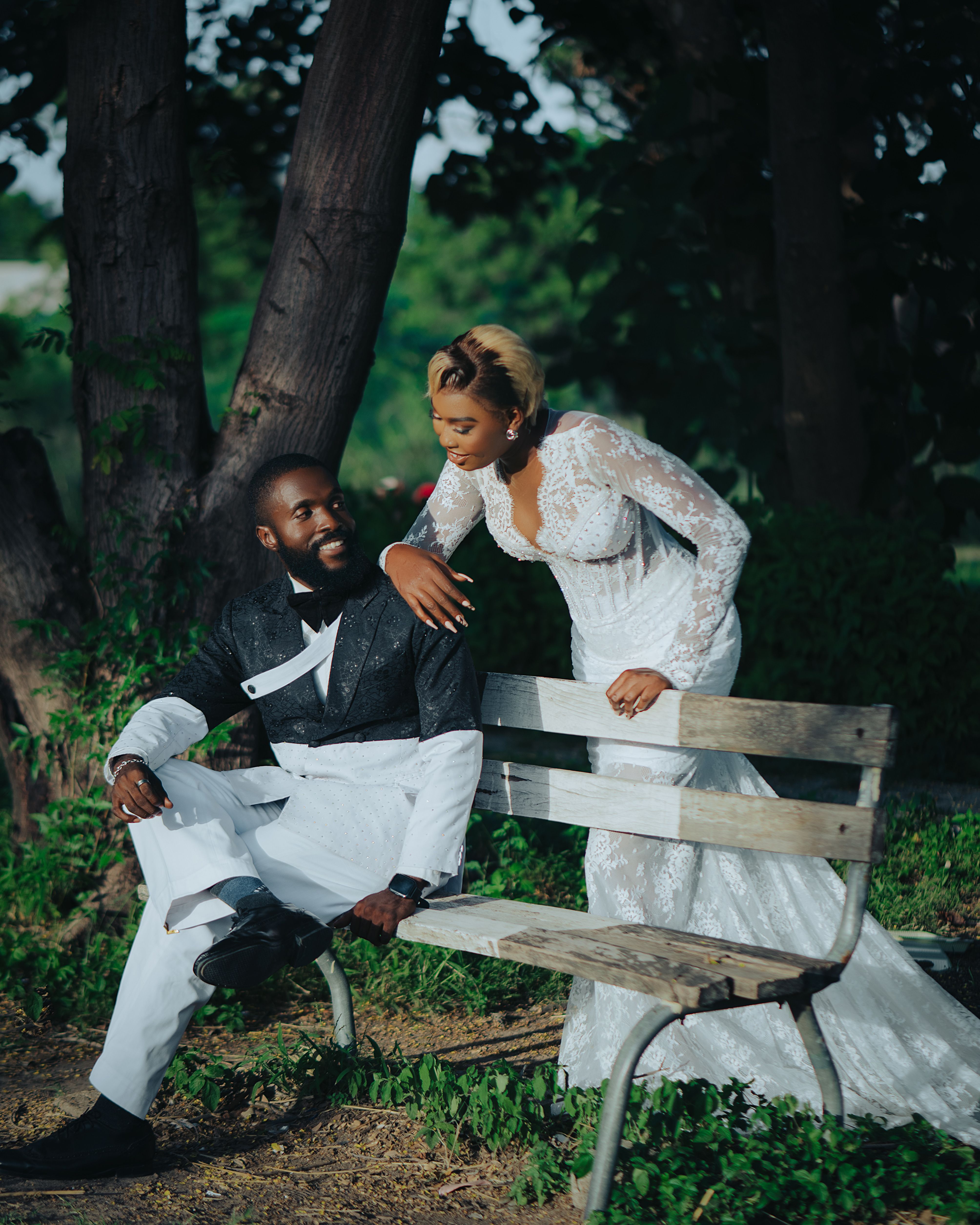 A joyful couple in wedding attire sharing a moment on a park bench outdoors.
