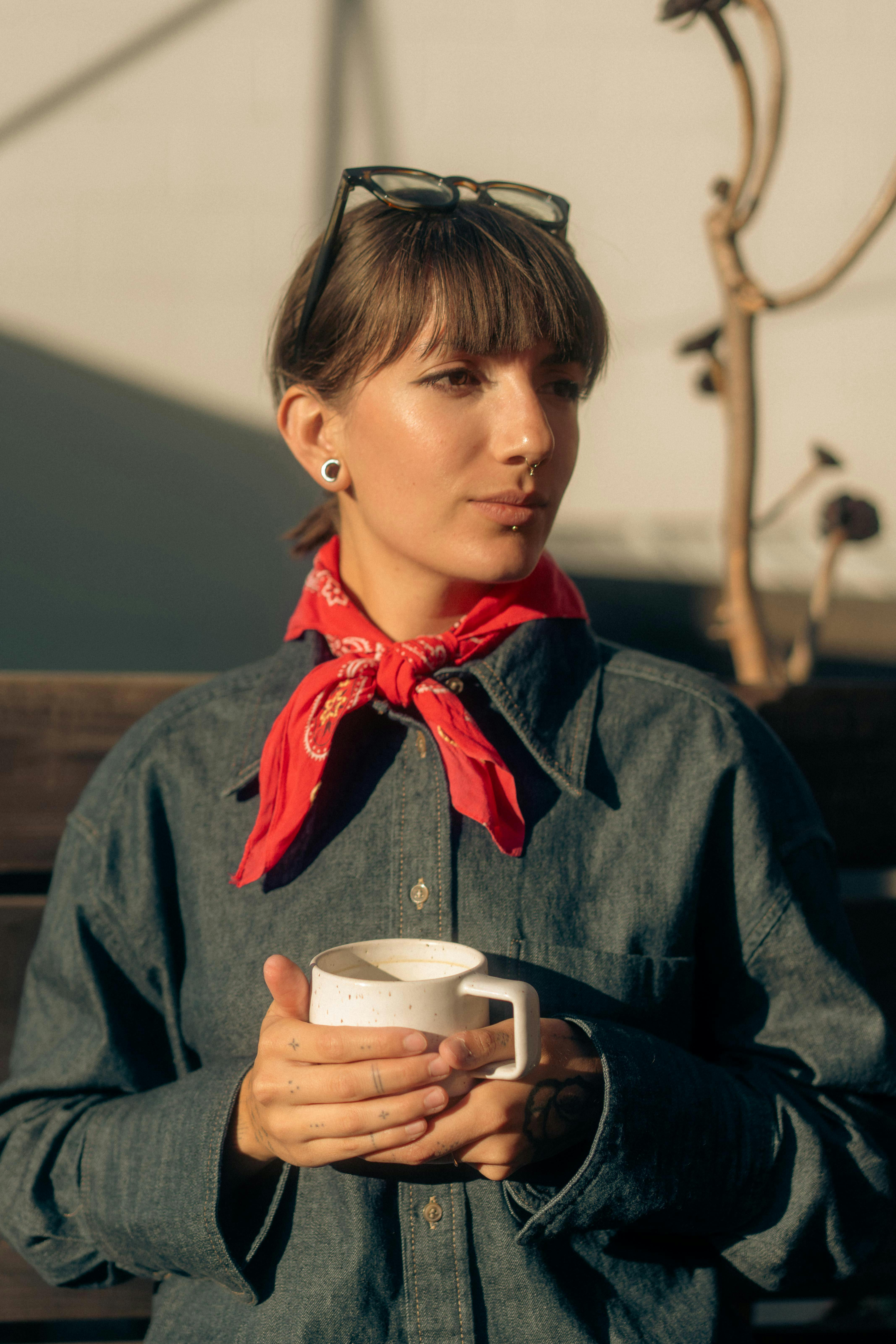 免費 戴著紅色圍巾的年輕女子在戶外陽光下享用一杯咖啡。 圖庫相片